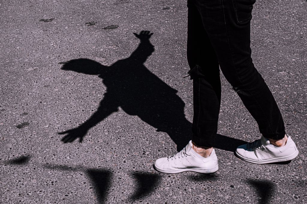 A photograph of a person's shadow. It makes them appear to be balancing off a string of flags.